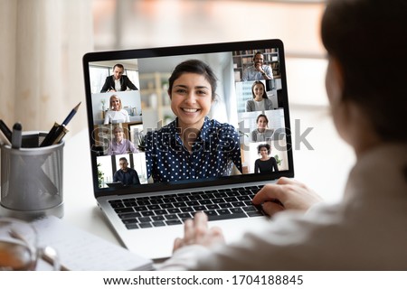 Woman sit at desk looking at computer screen where collage of diverse people webcam view. Indian ethnicity young woman lead video call distant chat, group of different mates using videoconference app
