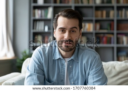 Head shot millennial guy sit on sofa in living room makes video call looks at camera, conversation by distant videocall, distance hiring job interview process, tutor and trainee study on-line concept