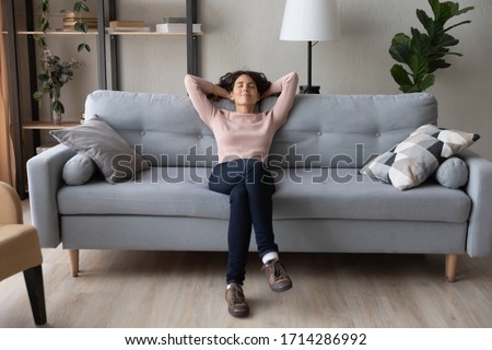 Front full length view tranquil millennial pretty woman relaxing on comfortable sofa in living room. Peaceful young lady sleeping, reducing stress, enjoying lazy weekend time on sofa alone at home.