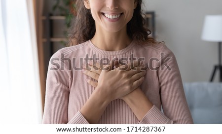 Close up focus on happy sincere female holding folded hands on chest. Emotional positive kind candid millennial woman feeling thankful indoors, showing gratitude sign, believe faith charity concept. 商業照片 © 