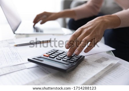 Close up focus on female hands making calculations. Young woman looking through paper bills, managing monthly household expenses and incomes, using e-banking application, planning investments.
