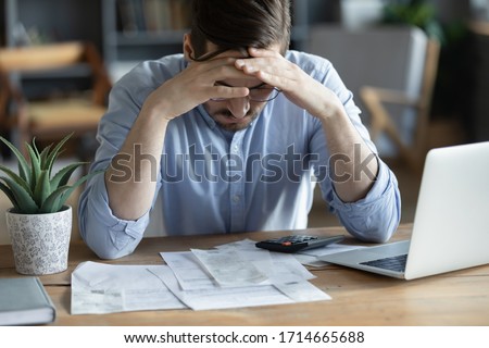 Sad depressed man checking bills, anxiety about debt or bankruptcy, financial problem, bank debt or lack of money, unhappy frustrated young male sitting at work desk with laptop and calculator Foto stock © 