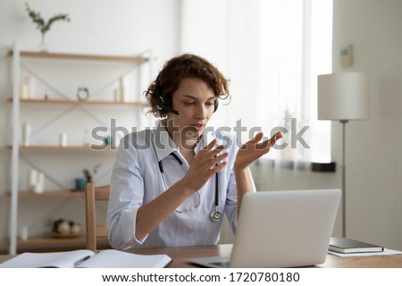 Female general practitioner wears white coat and headset speaking videoconferencing on laptop computer using online video call consultation app. Remote medical help for distance patient, telemedicine. ストックフォト © 