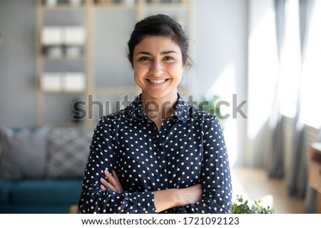 Head shot portrait smart confident smiling millennial indian woman standing with folded arms at home. Attractive young hindu teenager student girl freelancer looking at camera, posing for photo.