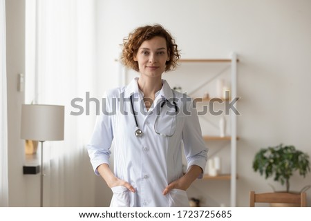 Confident young female physician standing in medical office. Proud professional woman doctor therapist looking at camera. Portrait of lady general practitioner wearing white coat and stethoscope. ストックフォト © 