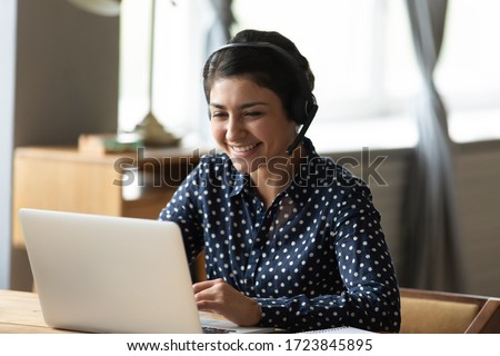 Head shot attractive happy friendly indian woman sitting at desk, holding video call with friends at home. Smiling young mixed race hotline specialist helping customers remotely at workplace.