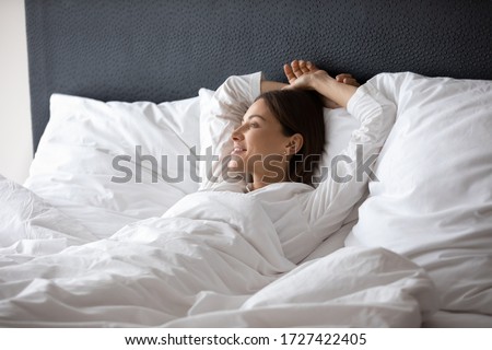 Woman wake up lying in bed dreaming planning day enjoy good morning vacation in hotel bedroom. Carefree 30s female relish comfy rest, warm duvet, put head behind head breath fresh air relaxing at home Foto stock © 