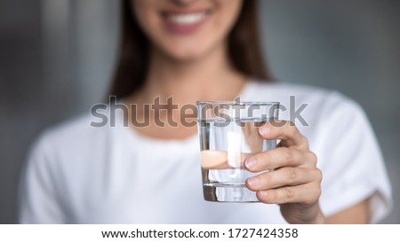 Horizontal banner image, on foreground caucasian female hand holds glass of clear water give to camera smiling selective close up focus. Concept of healthy lifestyle, beauty skin health care treatment