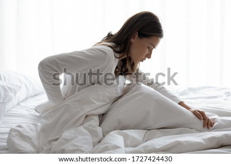 Side view of millennial woman woke up sitting in bed, unhealthy female woke up feels severe lower back pain during period, pinched nerve discomfort in vertebrae, herniated spinal disc symptoms concept Photo stock © 