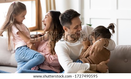 Excited parents having fun with two little daughters at home, cute preschool girls with loving happy mother and father sitting on couch at home, hugging and laughing, family spending weekend together