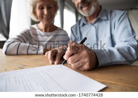Close up focus on wrinkled male hand signing paper document. Smiling elderly mature family couple putting signature on leasing or medical insurance contract, purchase agreement with real estate agent Imagine de stoc © 