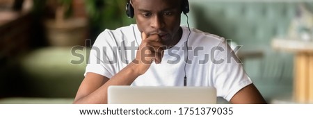 Focused African student wear headphones studying on-line do exercise using laptop, watching video, learning language, self-education, e-study concept. Horizontal photo banner for website header design Foto d'archivio © 