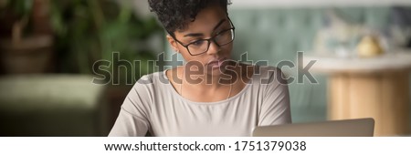 Horizontal photo banner for website header design, African student girl wear glasses sit indoors look at pc screen study on-line, do assignment, prepare for university admission exams, e-study concept