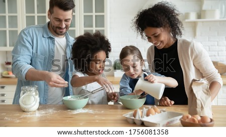 Full multi ethnic family with adorable daughters gathered in modern kitchen cooking pancakes together. Cake mix preparation, make yummy home-made dessert, enjoy communication and cookery hobby concept Stock foto © 