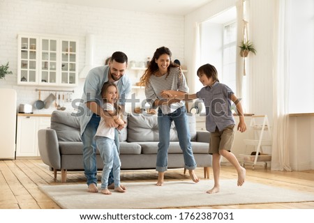 Happy family playing funny game having fun together with little son and daughter in modern living room. Young dad and mother with adorable cute children doing exercises, enjoying weekend at home.