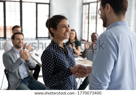 Happy proud excited Indian ethnicity employee get promotion receive praises from boss and cheering and congratulations from diverse staff members shake hands with chief. Recognition of success concept
