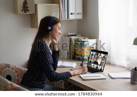 Smiling Caucasian female employee in headphones sit at desk at home talk on video call with colleagues, young woman have online webcam conversation virtual event with diverse multiethnic coworkers