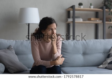 Sad young Caucasian woman sit on couch at home look in distance mourning yearning, unhappy upset female thinking suffering from relationships problems, struggle with miscarriage or abortion trouble