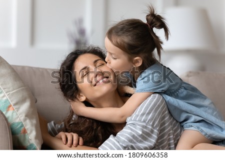 Little daughter gently cuddles kiss mother on cheek showing love and express caress resting on couch at home. Happy family, pleasure be mommy, mother day congratulations, sweet moment together concept