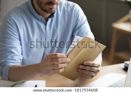 Crop close up of man sit at desk open envelope with paper letter or correspondence at office. Male worker get postal paperwork or notice notification at workplace, receive message or invitation.