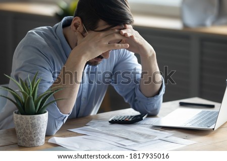 Distressed young Caucasian man sit at desk paying bills feel stressed having financial problems. Unhappy upset millennial male frustrated by debt or bankruptcy managing household budget or expenses.