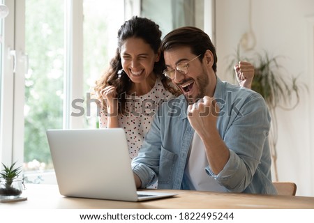 Overjoyed millennial man and woman triumph win online lottery on laptop. Happy excited young Caucasian couple feel euphoric with good email, get amazing sale offer or discount deal on computer.