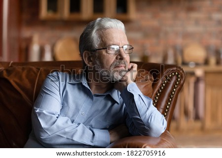 Pensive mature Caucasian grey-haired man relax on sofa in living room look in distance thinking dreaming. Thoughtful senior 70s grandfather rest on couch at home, lost in thoughts remembering missing.