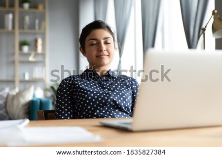 Serene indian business woman smiling sit at desk lean on office chair, enjoy break pause after working hard closing eyes daydreaming relaxing, feels satisfaction after project accomplishment concept 商業照片 © 