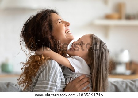 Close up side view overjoyed smiling young mother and daughter hugging and laughing, enjoying tender moment, happy mum and adorable preschool girl kid cuddling, having fun together at home