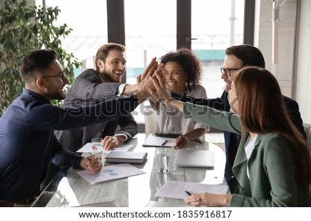 Overjoyed young mixed race business people sitting at table, joining hands in air, showing group unity, celebrating successful teamwork or professional achievement, raising team spirit at meeting. Photo stock © 