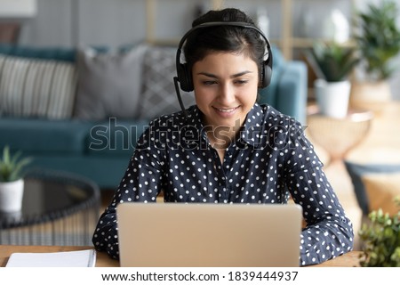 Attractive indian woman sit at homeoffice room wearing headset take part in educational webinar using laptop. Video call event with clients or personal chat with friend remotely concept