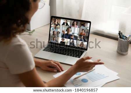 Back view of female employee talk speak on team video call with diverse colleagues coworkers. Woman worker have webcam digital virtual conference at home office, engaged in online group meeting.