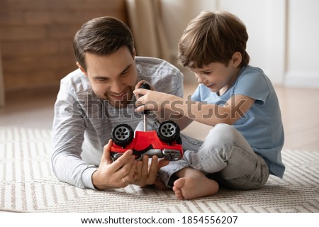 Close up cute adorable son repairing toy card with loving smiling father, playing on warm floor at home, little boy holding using screwdriver, having fun with dad, enjoying leisure time together