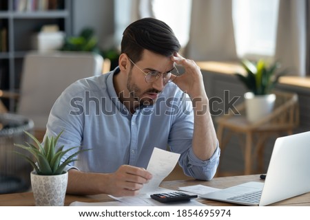Small business owner experiences financial crisis, high costs, bank debt, money overspend concept. Man sitting at desk looks at laptop screen holding receipt feels desperate after calculating expenses Foto stock © 