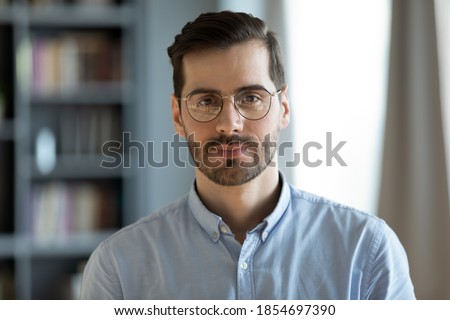 Head shot young attractive businessman in glasses standing in modern office pose for camera. Videoconference call profile picture handsome entrepreneur portrait, professional occupation person concept