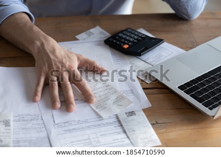 Individual entrepreneur make analysis of firm expenses, accountant do paperwork concept. On desk lot of receipts, calculator and laptop close up view. Man sit at table reviewing bills, managing budget