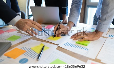 Close up of diverse businesspeople working on project startup presentation in team, comparing statistic data, studying values on graph diagrams, analyzing trends patterns, making notes on paper sheets