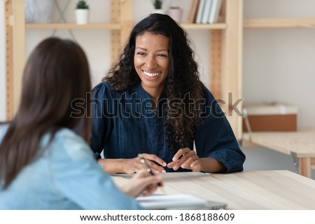 Smiling young African American woman talk with female colleagues brainstorm at office team meeting. Happy multiracial diverse colleagues speak discuss business ideas. Teamwork, collaboration concept.