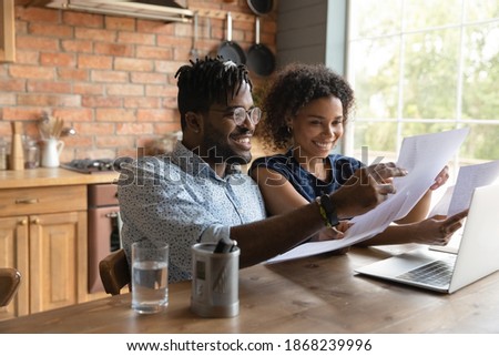 Happy 30s african ethnicity biracial family couple reading paper correspondence. doing financial paperwork, managing household budget, planning expenditures, feeling satisfied with enough money.