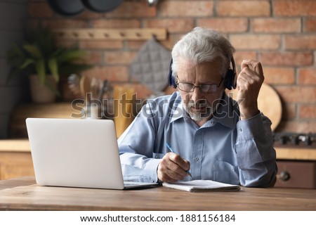 Focused middle aged mature man in glasses wearing headphones, involved in studying on online courses using computer applications. Concentrated older grandfather watching online webinar, writing notes. Photo stock © 
