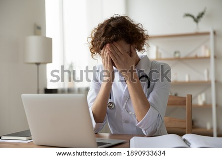 Anxious young female physician doctor covering face with hands, feeling nervous or exhausted at clinic office. Unhappy 35s general practitioner suffering from severe headache at hospital workplace. Foto d'archivio © 