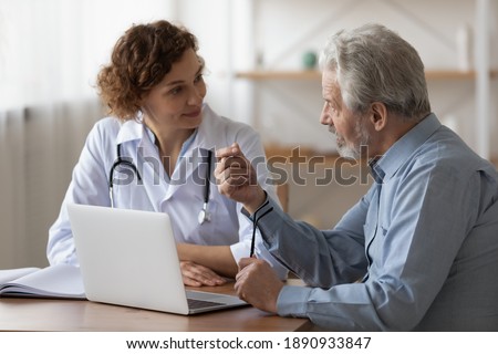 Serious middle aged retired man consulting with young female physician doctor at checkup meeting in hospital. Skilled general practitioner giving healthcare medical advices to mature patient.