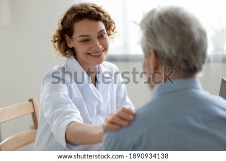 Happy young 30s beautiful physician doctor nurse supporting elderly mature retired patient, sharing good news about health test results, feeling satisfied with disease treatment at checkup meeting.