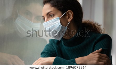 Upset young Caucasian woman in medical facial mask look in window feel lonely distressed sick with covid-19. Unhappy female in facemask suffer from coronavirus. Quarantine, corona pandemic concept. Foto stock © 