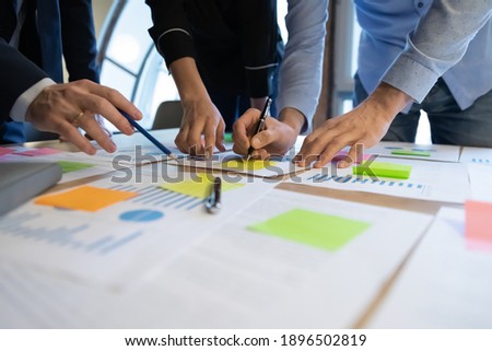 Close up diverse employees working on financial project statistics or report, writing notes on colorful sticky papers, checking documents, coworkers developing business strategy, teamwork