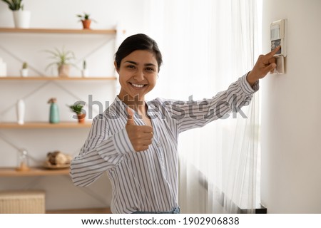 Portrait of smiling indian lady use domestic fire alarm system switch button on wall keypad show thumb up. Young female satisfied user of home security equipment look at camera trust recommend safety Stock photo © 