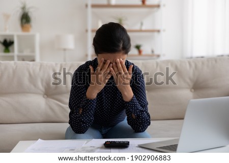 Sad stressed young indian female deal with bankruptcy of her small business having huge loan mortgage debt. Upset depressed mixed race woman crying at home office after losing money in fraudulent deal