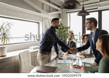 Diverse business partners shaking hand in modern boardroom after negotiation, signing contract, making successful deal, Arabian executive greeting new employee at meeting, group negotiations