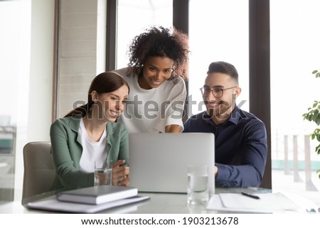 Three happy diverse colleagues working on project together, using laptop, sitting at table in office, discussing strategy, brainstorming, smiling African American businesswoman training staff Foto stock © 