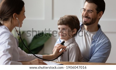 Caring woman doctor hold stethoscope listen to happy small boy patient heart chest in hospital. Young father with little son child do checkup examination at pediatrician in clinic. Healthcare concept.